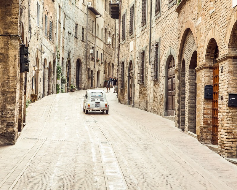 Art print of a classic Fiat 500 mini driving through an alley way in Tuscany